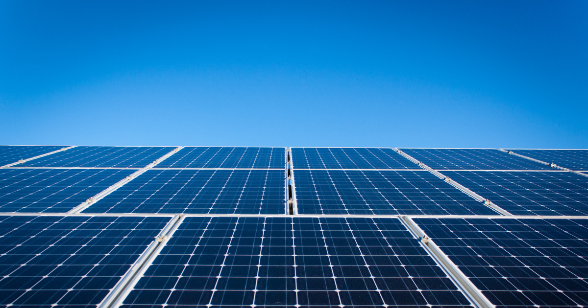  A imagem mostra fileiras de módulos solares fotovoltaicos sob um céu azul claro e sem nuvens. Representa energia limpa, sustentável e a captação eficiente da luz solar.