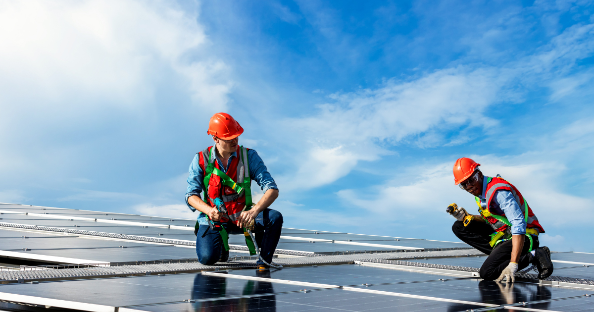  Dois profissionais instalam painéis solares no telhado, usando equipamentos de segurança. Eles trabalham em equipe para ajustar os módulos, sob um céu claro.