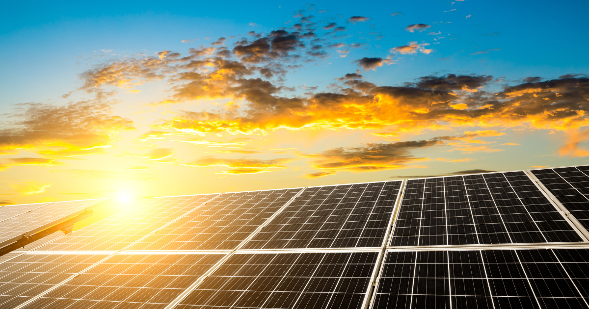  A imagem destaca painéis solares sob um céu azul com nuvens douradas e o sol ao fundo, simbolizando energia sustentável e renovável.