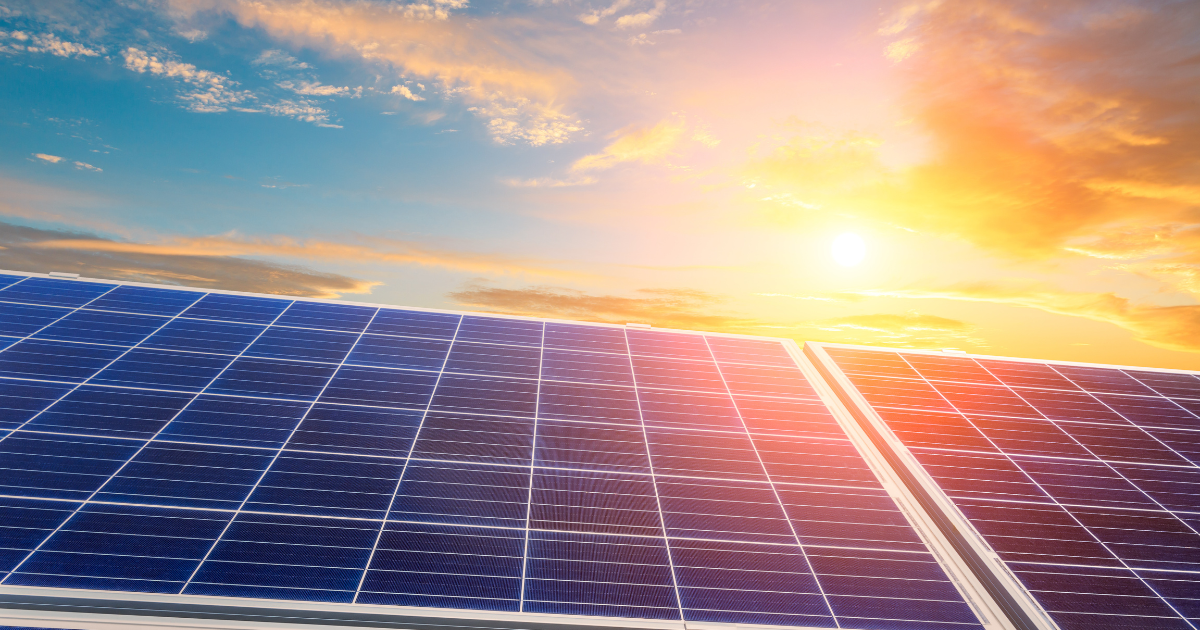 A imagem mostra painéis solares sob um céu azul com nuvens douradas e o sol ao fundo, simbolizando energia limpa e sustentável.