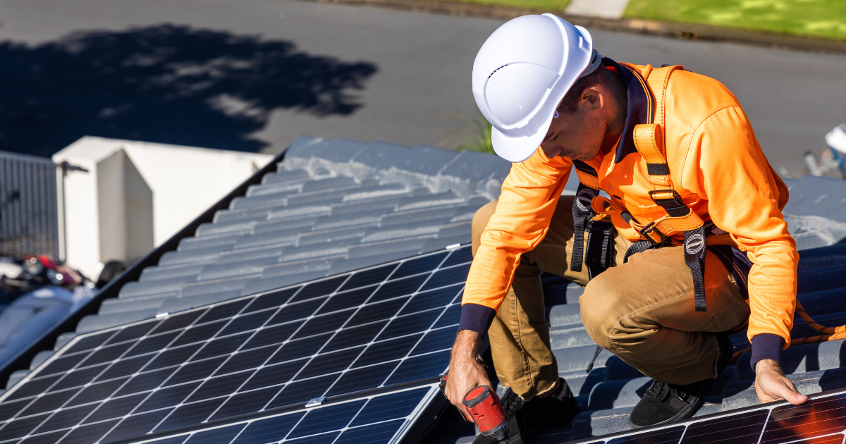  Integrador solar instalando painéis solares em um telhado, usando capacete, uniforme de alta visibilidade e cinto de segurança.