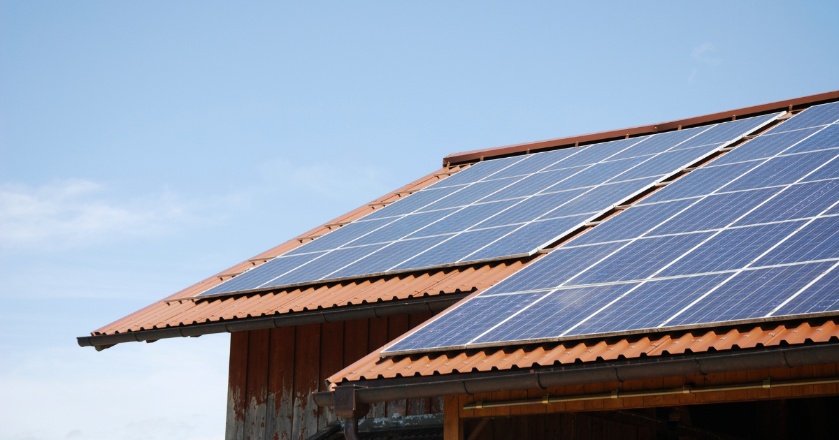  A imagem mostra um telhado com painéis solares instalados sobre telhas de barro marrom, em um dia ensolarado com céu azul.