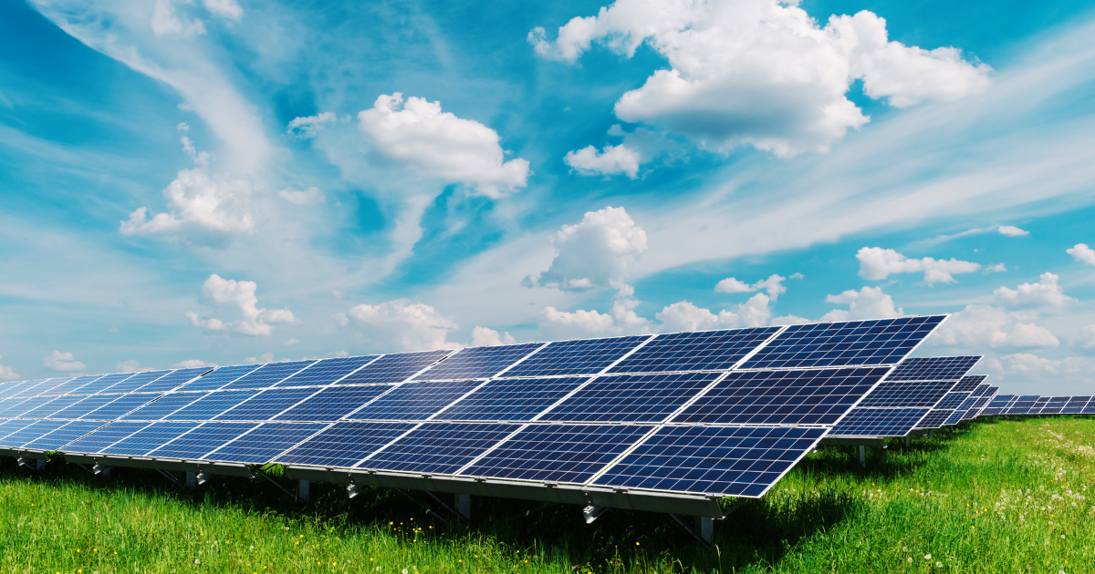 Campo de painéis solares em um gramado verde sob um céu azul com nuvens, destacando a energia solar como fonte sustentável e limpa.